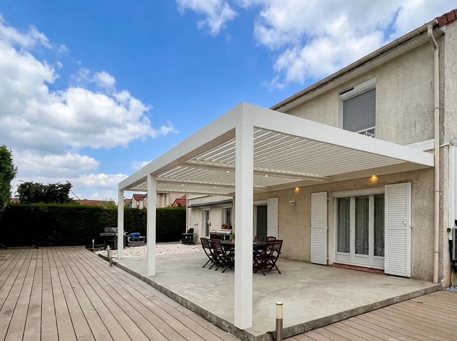 Terrasse extérieure résidentielle avec pergola bioclimatique à lames orientables en aluminium laqué blanc, fixée en appui mural