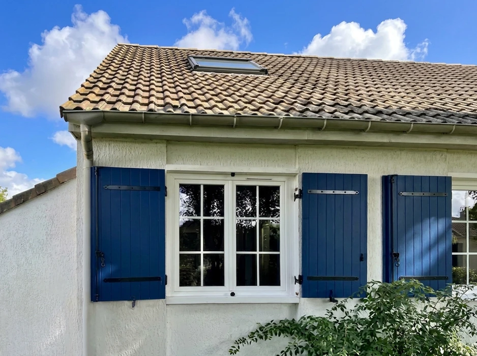 Façade de maison de style français, crépi blanc, volets battants en bois peints bleu marine, fenêtre à croisillons avec cadre PVC blanc