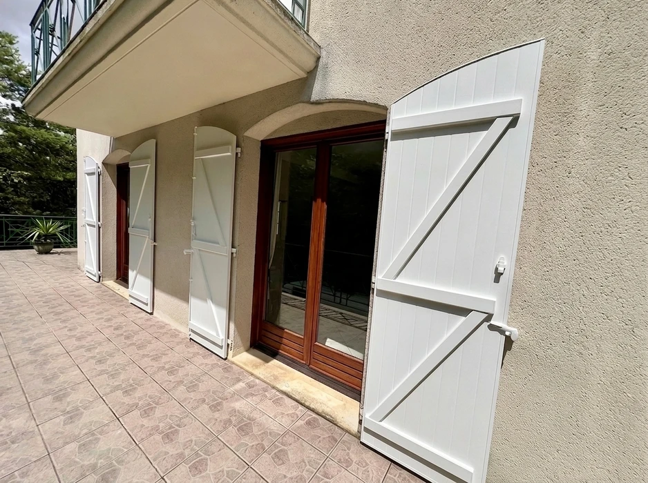 Façade extérieure en enduit grésé beige avec volets battants fermés en aluminium gris anthracite, style lisse à lames horizontales