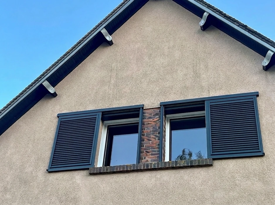Façade extérieure en enduit grésé beige avec volets battants fermés en aluminium gris anthracite, style lisse à lames horizontales