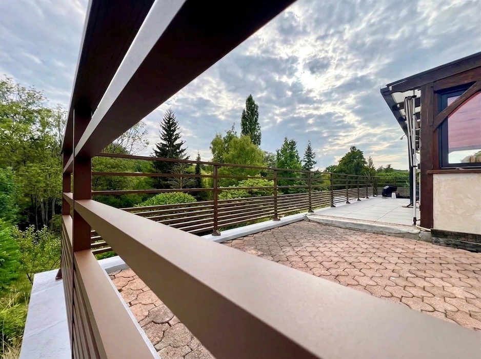 Terrasse couverte vue de l'intérieur, pergola bioclimatique à lames orientables en aluminium blanc, position ouverte laissant apparaître un ciel bleu nuageux